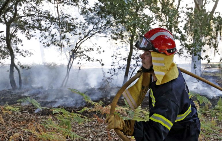 Un bombero carga con la manguera tras la extinción de un incendio forestal cerca de unas viviendas en Cacheiras, en la localidad de Teo (A Coruña) Un bombero carga con la manguera tras la extinción de un incendio forestal cerca de unas viviendas en Cacheiras, en la localidad de Teo (A Coruña)