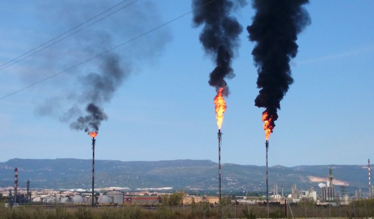Pla obert amb les dos torxes de Repsol i Dow a l'esquerra amb les denses columnes de fum negre visibles a molts quilòmetres. Pla obert amb les dos torxes de Repsol i Dow a l'esquerra amb les denses columnes de fum negre visibles a molts quilòmetres.