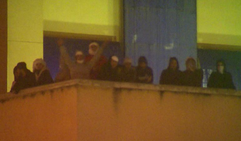Fotografía capturada de imágenes de EFE TV. Unos 30 inmigrantes continúan en la azotea del Centro de Internamiento de Extranjeros (CIE) de Aluche más de once horas después de iniciar un motín en el edificio, situado en la madrileña avenida de los Poblados, mientras que la Policía Nacional ha intentado negociar sin éxito con los internos. Los internos permanecen recluidos en la terraza de la parte superior del CIE, aunque solo unos pocos son visibles desde la calle, y algunos portan palos y pancartas hechas en tela en las que se puede leer "libertad". Fotografía capturada de imágenes de EFE TV. Unos 30 inmigrantes continúan en la azotea del Centro de Internamiento de Extranjeros (CIE) de Aluche más de once horas después de iniciar un motín en el edificio, situado en la madrileña avenida de los Poblados, mientras que la Policía Nacional ha intentado negociar sin éxito con los internos. Los internos permanecen recluidos en la terraza de la parte superior del CIE, aunque solo unos pocos son visibles desde la calle, y algunos portan palos y pancartas hechas en tela en las que se puede leer "libertad".