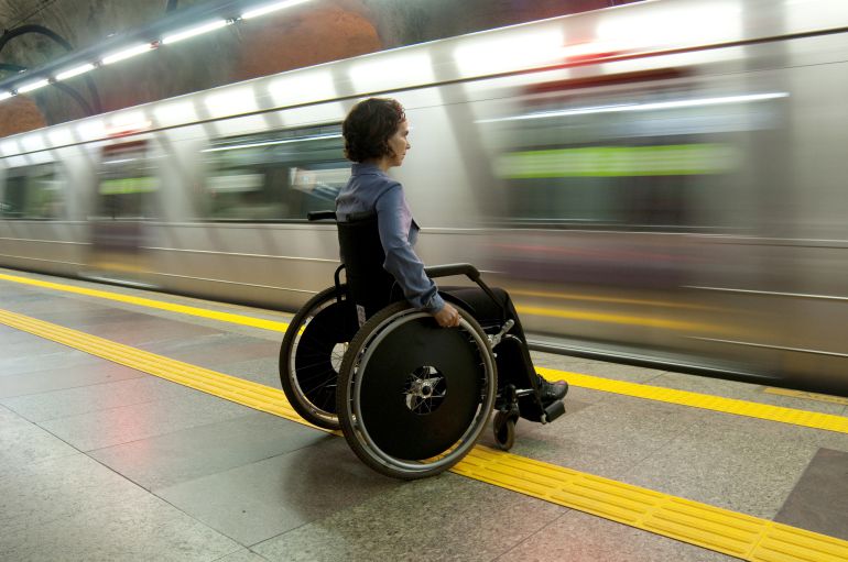 Un tren pasa de largo frente a una mujer en silla de ruedas