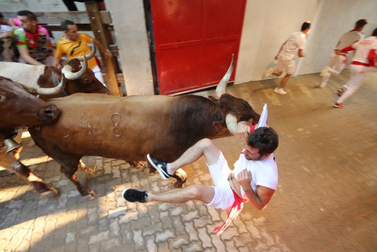 Encierro de Sanfermines. Corredor colgando por el pañuelo de un miura. Encierro de Sanfermines. Corredor colgando por el pañuelo de un miura.