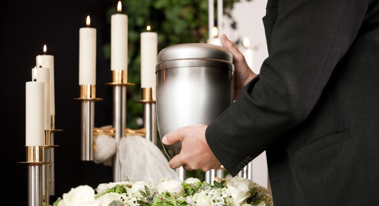 Imagen de un hombre sosteniendo una urna funeraria rodeado de velas y flores. Imagen de un hombre sosteniendo una urna funeraria rodeado de velas y flores.