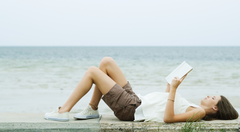 Una chica lee un libro tumbada en un muro frente al mar. Una chica lee un libro tumbada en un muro frente al mar.