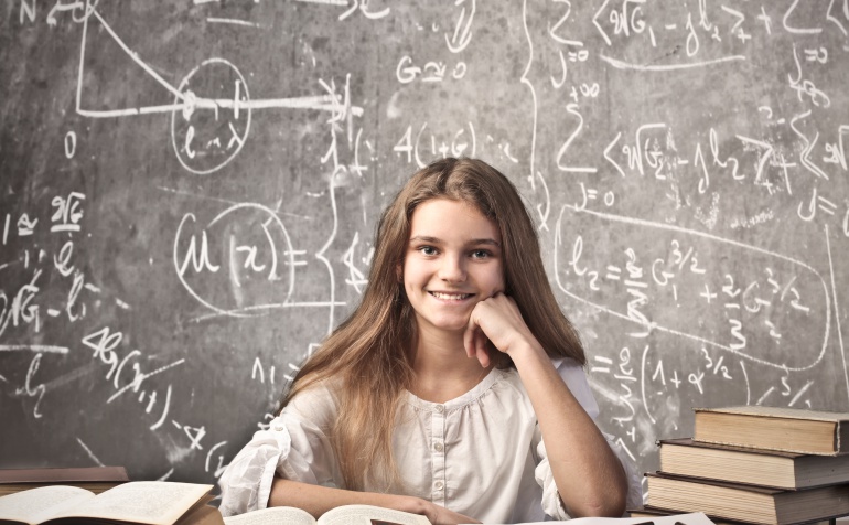 Imagen de una niña rodeada de libros delante de una pizarra llena de ecuaciones y fórmulas matemáticas. Imagen de una niña rodeada de libros delante de una pizarra llena de ecuaciones y fórmulas matemáticas.