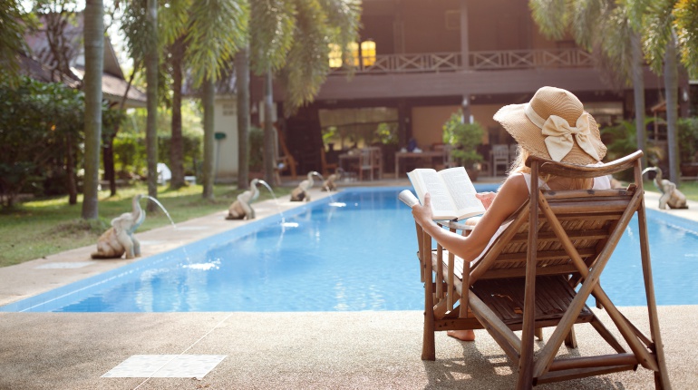 Imagen de una mujer leyendo en una tumbona frente a la piscina de una mansión. Imagen de una mujer leyendo en una tumbona frente a la piscina de una mansión.