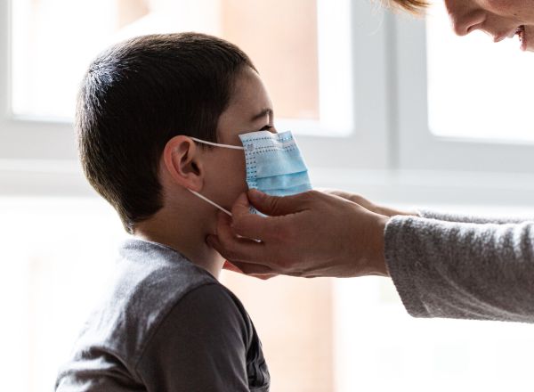 Una madre coloca a su hijo una mascarilla