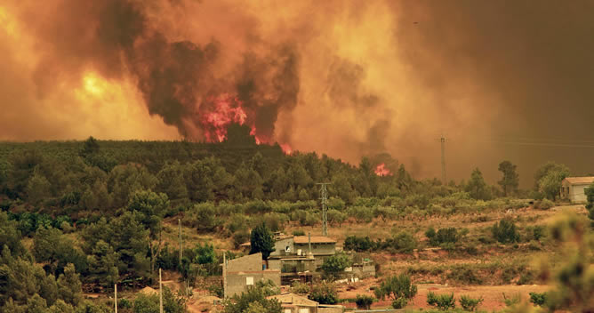 Las llamas se aproximan a un conjunto de viviendas en la localidad valenciana de Turis, uno de los cinco municipios afectados por el incendio forestal declarado este jueves en la localidad de Cortes de Pallás