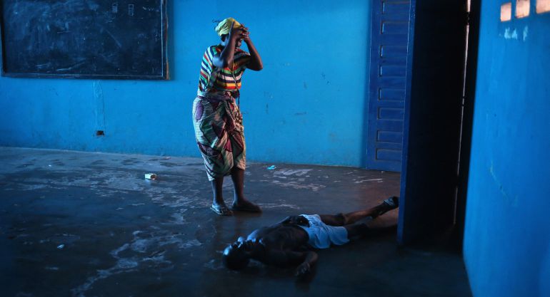 MONROVIA, LIBERIA - AUGUST 15: Umu Fambulle stands over her husband Ibrahim after he staggered and fell, knocking him unconscious in an Ebola ward on August 15, 2014 in Monrovia, Liberia. People suspected of contracting the Ebola virus are being sent by Liberian health workers to the center, a closed primary school originally built by USAID. The Ebola epidemic has killed more than 1,000 people in four West African countries. (Photo by John Moore/Getty Images) *** BESTOF2014 *** YEARINREVIEW *** MONROVIA, LIBERIA - AUGUST 15: Umu Fambulle stands over her husband Ibrahim after he staggered and fell, knocking him unconscious in an Ebola ward on August 15, 2014 in Monrovia, Liberia. People suspected of contracting the Ebola virus are being sent by Liberian health workers to the center, a closed primary school originally built by USAID. The Ebola epidemic has killed more than 1,000 people in four West African countries. (Photo by John Moore/Getty Images) *** BESTOF2014 *** YEARINREVIEW ***