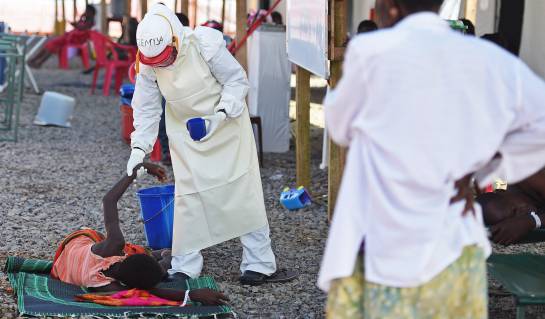 A health worker wearing protective equipment assists an Ebola patient at the Kenama treatment centre run by the Red Cross Society on November 15, 2014. Ebola-hit Sierra Leone faces social and economic disaster as gains made since the country's ruinous civil war are wiped out by the epidemic, according to a major study released on November 15, 2014. Ebola has killed more than 5,000 people, mostly in Guinea, Liberia and Sierra Leone, and is expected to hit economic growth in the region, as border closures and stigma disrupt the flow of goods and people. AFP PHOTO/ FRANCISCO LEONG A health worker wearing protective equipment assists an Ebola patient at the Kenama treatment centre run by the Red Cross Society on November 15, 2014. Ebola-hit Sierra Leone faces social and economic disaster as gains made since the country's ruinous civil war are wiped out by the epidemic, according to a major study released on November 15, 2014. Ebola has killed more than 5,000 people, mostly in Guinea, Liberia and Sierra Leone, and is expected to hit economic growth in the region, as border closures and stigma disrupt the flow of goods and people. AFP PHOTO/ FRANCISCO LEONG