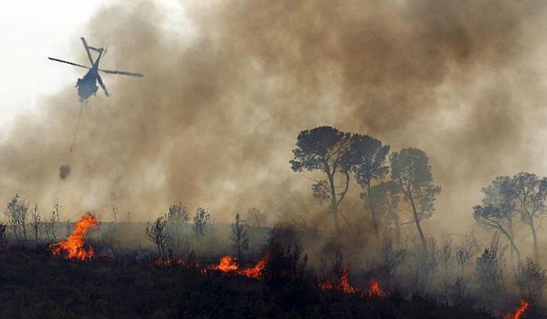 Un helicóptero rocía de agua una zona en llamas. Un helicóptero rocía de agua una zona en llamas.