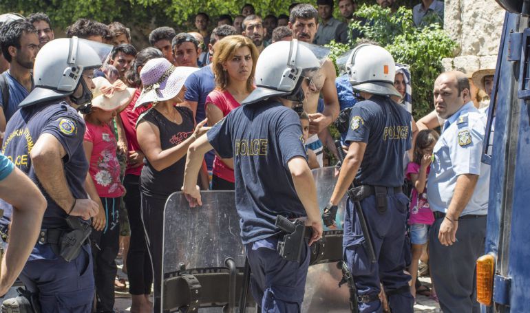 Varios policías vigilan a los inmigrantes que esperan en fila delante de la comisaría de la isla de Kos, Grecia. Varios policías vigilan a los inmigrantes que esperan en fila delante de la comisaría de la isla de Kos, Grecia.