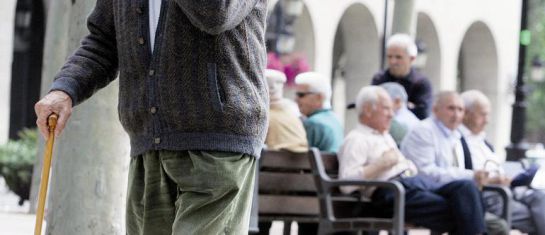 Un pensiona camina en primer plano mientras otros permanecen sentados en un banco Un pensiona camina en primer plano mientras otros permanecen sentados en un banco