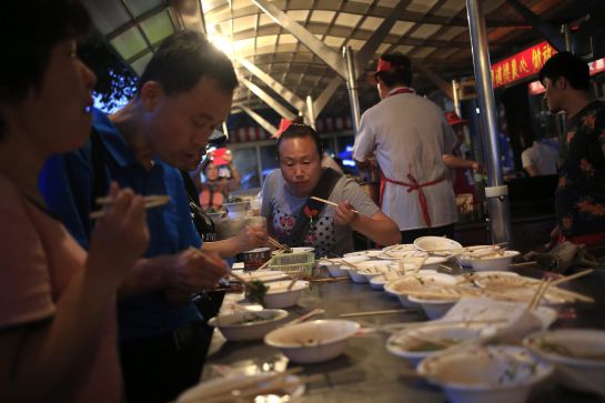 Varios visitantes cenan en un puesto en el mercado nocturno de Donghuamen. Varios visitantes cenan en un puesto en el mercado nocturno de Donghuamen.