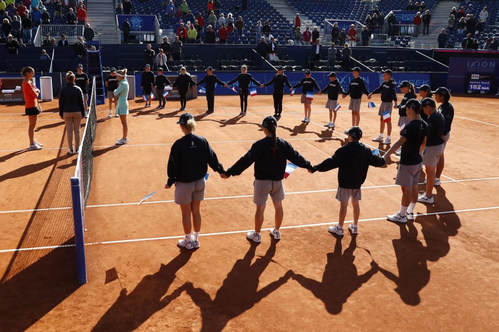 La tenista suiza Timea Bacsinszky y la luxemburguesa Mandy Minella se rodean por los recogepelotas que forman una cadena humana sosteniendo banderas francesas mientras guardan un minuto de silencio en memoria de las víctimas de la masacre de Niza. La tenista suiza Timea Bacsinszky y la luxemburguesa Mandy Minella se rodean por los recogepelotas que forman una cadena humana sosteniendo banderas francesas mientras guardan un minuto de silencio en memoria de las víctimas de la masacre de Niza.