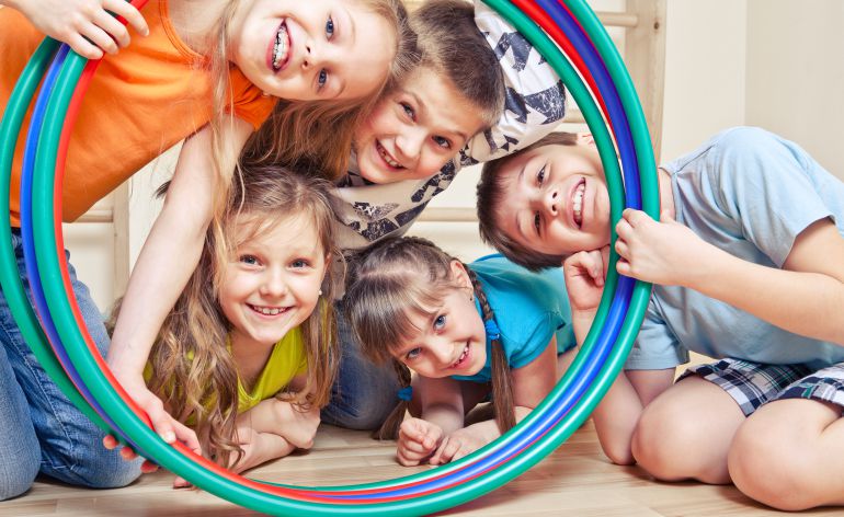 Un grupo de niños observa sonriente a través de varios aros de juego. Un grupo de niños observa sonriente a través de varios aros de juego.