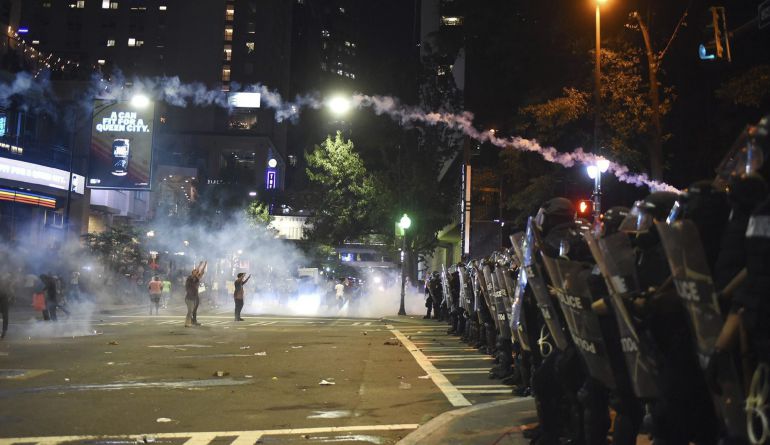 Dos manifestantes se encaran a policías antidisturbios con los brazos en alto durante unos disturbios en Charlotte en Carolina del Norte.