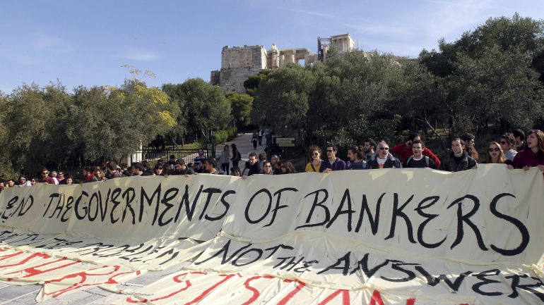 Manifestantes y afiliados a la Coalición de Izquierda radical (SYRIZA) sostienen una pancarta en la que se lee "Acabemos con el gobierno de los bancos. La austeridad es el problema, no la respuesta" durante una protesta en la entrada de la Avcrópolis en Atenas en noviembre de 2011. Manifestantes y afiliados a la Coalición de Izquierda radical (SYRIZA) sostienen una pancarta en la que se lee "Acabemos con el gobierno de los bancos. La austeridad es el problema, no la respuesta" durante una protesta en la entrada de la Avcrópolis en Atenas en noviembre de 2011.