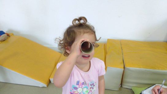 Una niña mira a través de un cilindro de cartón.