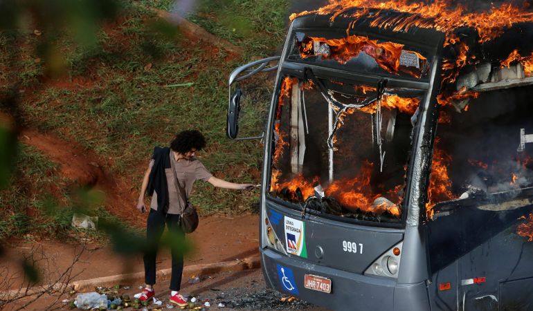 Un hombre se enciende un cigarrillo con las llamas de un autobús quemado por manifestantes contrarios al gobierno de Brasil. Un hombre se enciende un cigarrillo con las llamas de un autobús quemado por manifestantes contrarios al gobierno de Brasil.