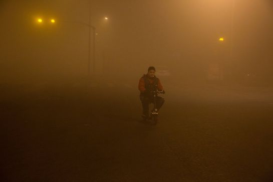 Un hombre fuma mietras monta en bici rodeado de polución en Pekín. Un hombre fuma mietras monta en bici rodeado de polución en Pekín.