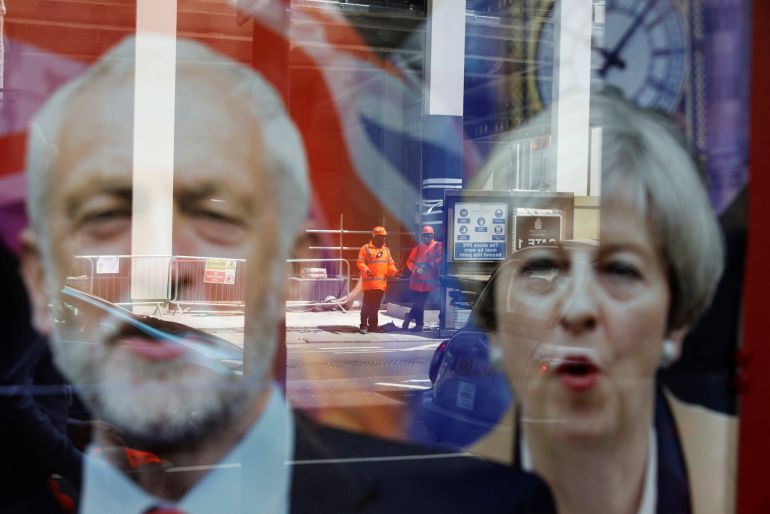 Trabajadores reflejados en una ventana sobre los carteles electorales de Theresa May y Jeremy Corbyn Trabajadores reflejados en una ventana sobre los carteles electorales de Theresa May y Jeremy Corbyn