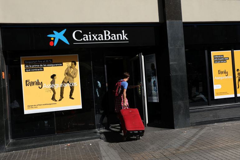 A hombre entra con una maleta en una oficina de Caixabank en Barcelona A hombre entra con una maleta en una oficina de Caixabank en Barcelona