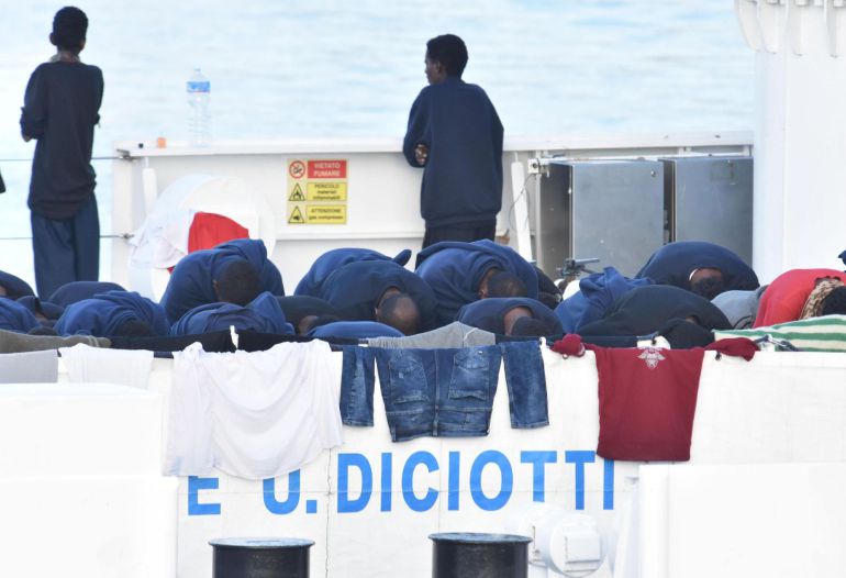 Migrantes rezan a la espera del desembarco del barco italiano de la Guardia Costera italiana en Catania, Italia. Migrantes rezan a la espera del desembarco del barco italiano de la Guardia Costera italiana en Catania, Italia.