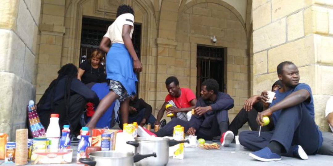 Persona migrantes recibiendo alimentos de la Red de Acogida Ciudadana en los arkupes del Ayuntamiento de Irun.