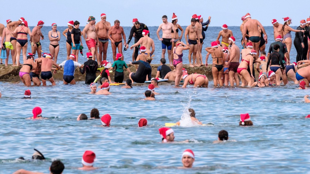 Un centenar de 'Papá Noeles' en bañador nadan hasta La Barra de Las Canteras