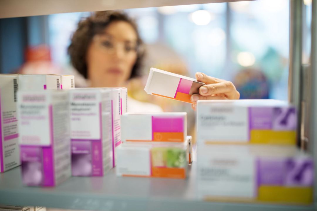 Una farmacéutica busca un medicamento en una estantería. Una farmacéutica busca un medicamento en una estantería.