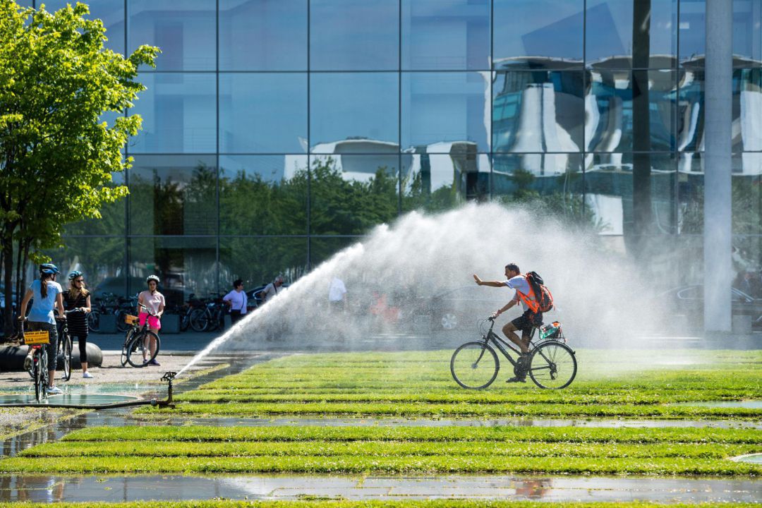 Un hombre en bicicleta se refresca con el agua de unos aspersores. Un hombre en bicicleta se refresca con el agua de unos aspersores.
