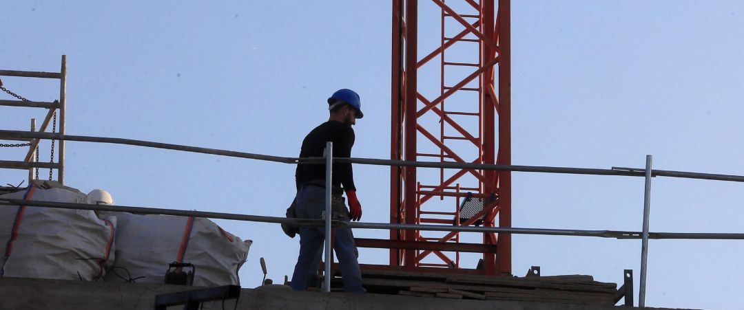 Un obrero permanece junto a una grúa de construcción Un obrero permanece junto a una grúa de construcción