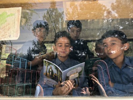 Unos niños leen libros al lado de los ventanales del autobús-biblioteca Unos niños leen libros al lado de los ventanales del autobús-biblioteca