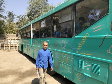 Un niño pasea por delante del autobús-biblioteca verde Un niño pasea por delante del autobús-biblioteca verde