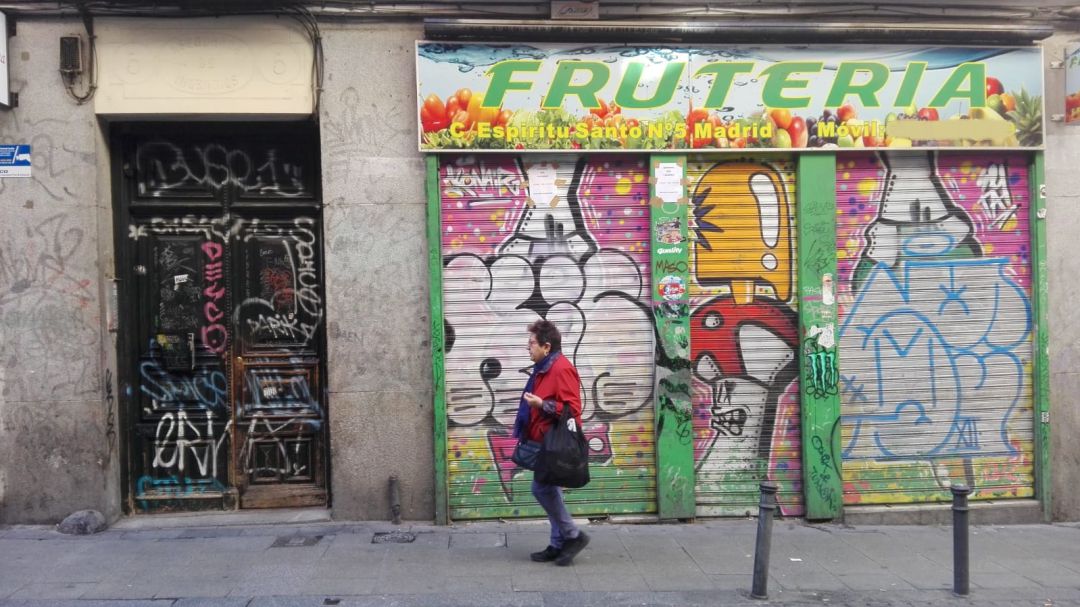 Una mujer pasa por delante de un portal y un comercio llenos de pintadas y firmas en Malasaña. Una mujer pasa por delante de un portal y un comercio llenos de pintadas y firmas en Malasaña.
