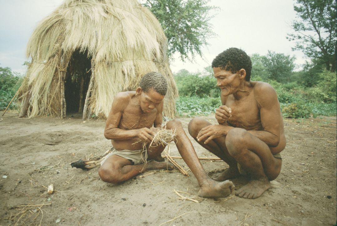 Un par de miembros de una tribu encienden un incendio fuera de una casa de césped tradicional en las colinas de Tsodilo, Botswana, 1985 Un par de miembros de una tribu encienden un incendio fuera de una casa de césped tradicional en las colinas de Tsodilo, Botswana, 1985