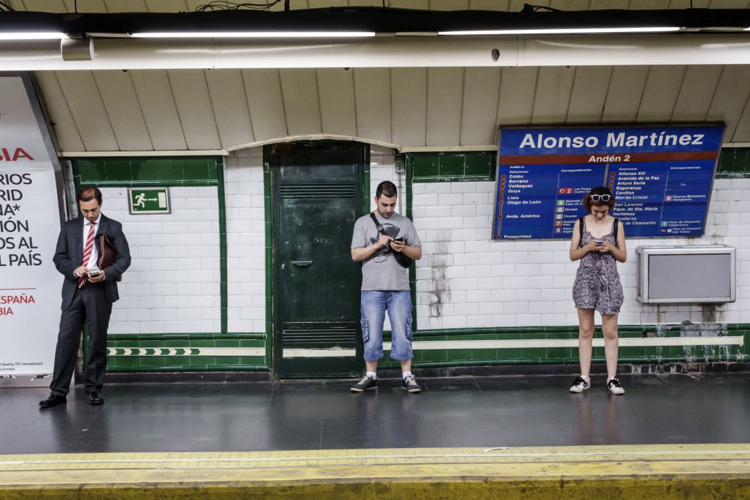 Varios ciudadanos miran el móvil mientras esperan la llegada del metro en la estación de Alonso Martínez Varios ciudadanos miran el móvil mientras esperan la llegada del metro en la estación de Alonso Martínez