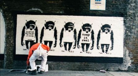 Banksy de espaldas mientras pinta uno de sus murales Banksy de espaldas mientras pinta uno de sus murales