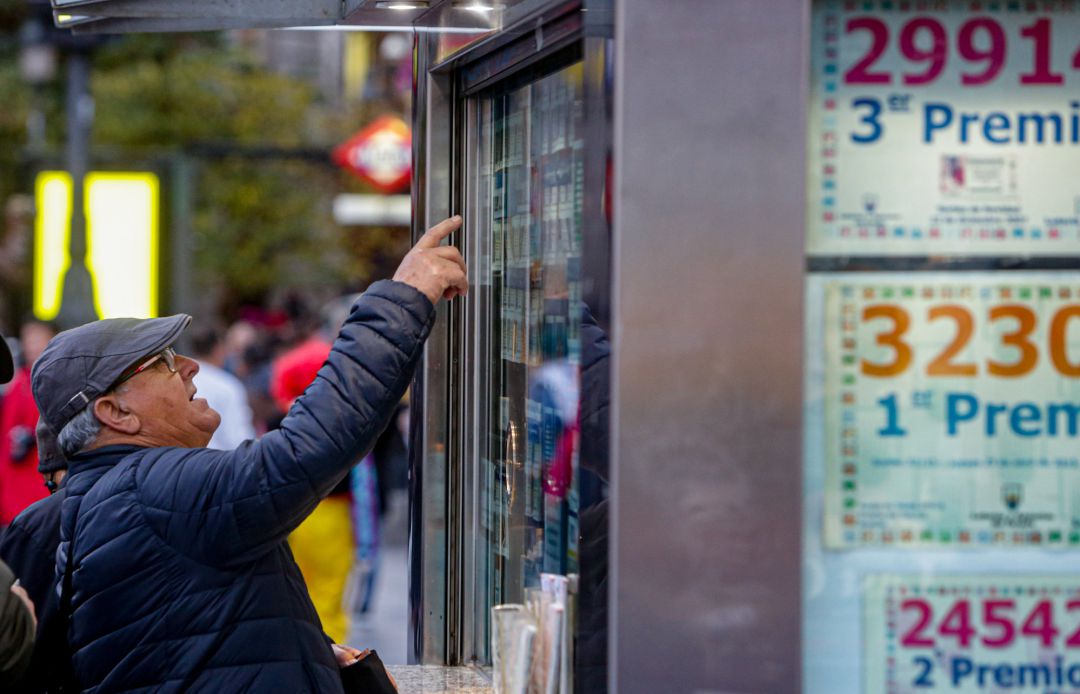 Un hombre consulta varios décimos en una administración de lotería. Un hombre consulta varios décimos en una administración de lotería.