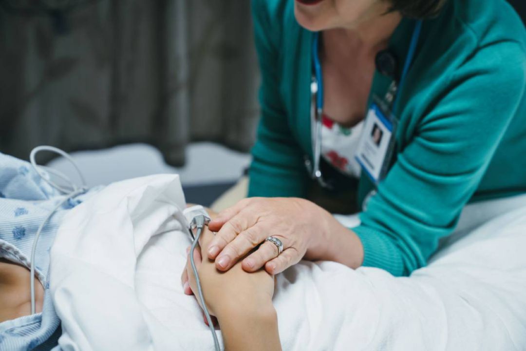 Una profesional sanitaria consuela a una paciente hospitalizada. Una profesional sanitaria consuela a una paciente hospitalizada.