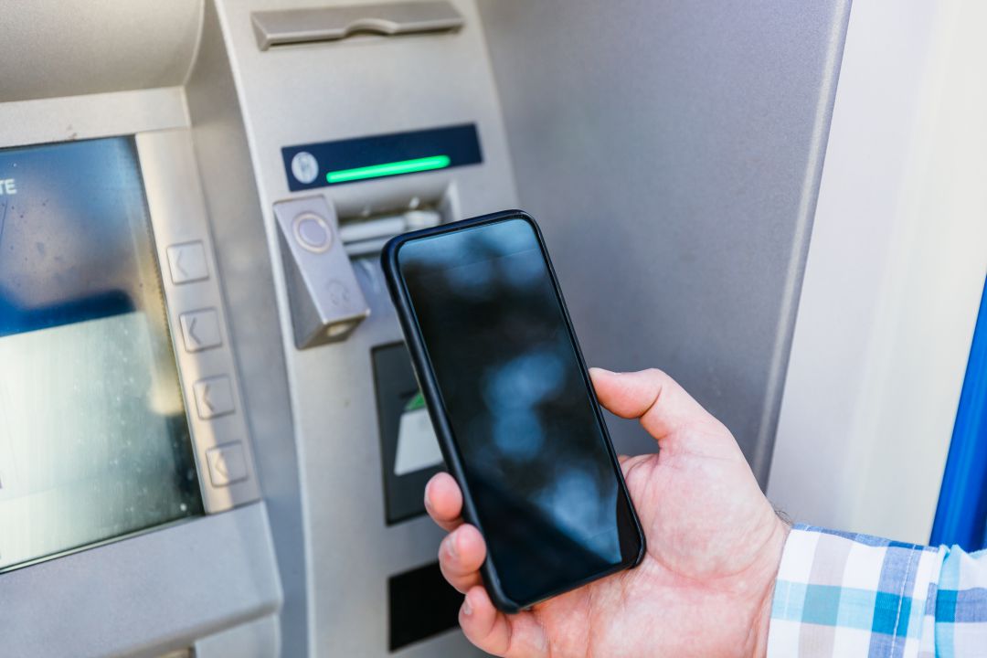 Un usuario utilizando el teléfono móvil para sacar dinero de un cajero Un usuario utilizando el teléfono móvil para sacar dinero de un cajero