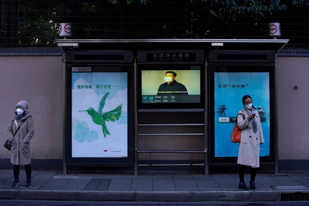Una mujer lleva mascarilla delante de una televisión donde se ve al presidente Xi Jinping con otra Una mujer lleva mascarilla delante de una televisión donde se ve al presidente Xi Jinping con otra