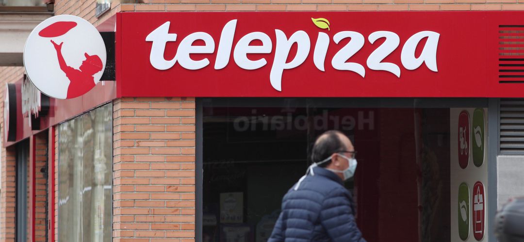 Un hombre protegido con mascarilla pasea cerca de un local de Telepizza Un hombre protegido con mascarilla pasea cerca de un local de Telepizza