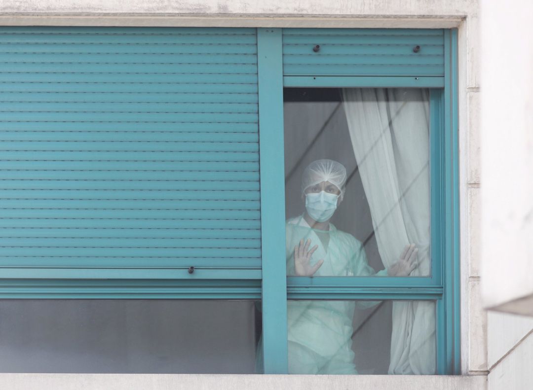 Una trabajadora del personal sanitario protegida con mascarilla se asoma por una de las ventanas de la Residencia ORPEA Madrid Una trabajadora del personal sanitario protegida con mascarilla se asoma por una de las ventanas de la Residencia ORPEA Madrid