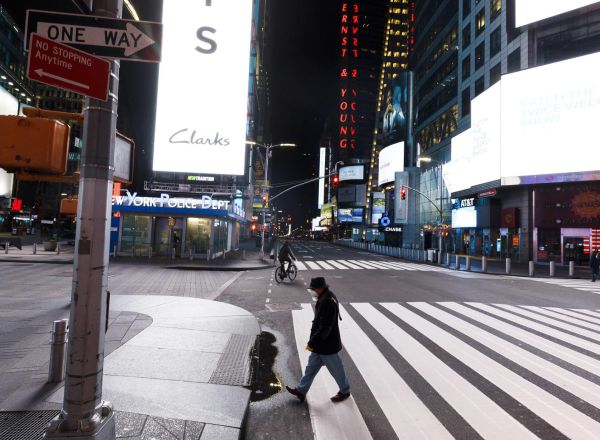 Varias personas caminan protegidas con mascarilla por una casi desierta Times Square.