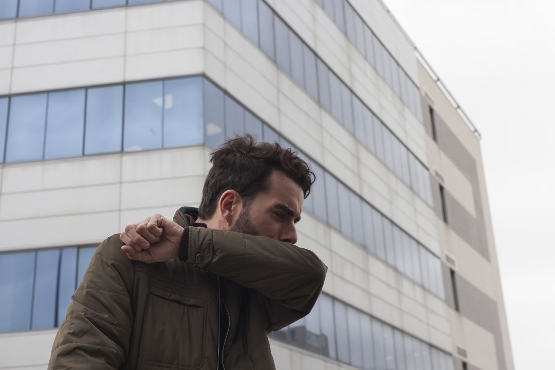 Hombre tosiendo en su brazo Hombre tosiendo en su brazo