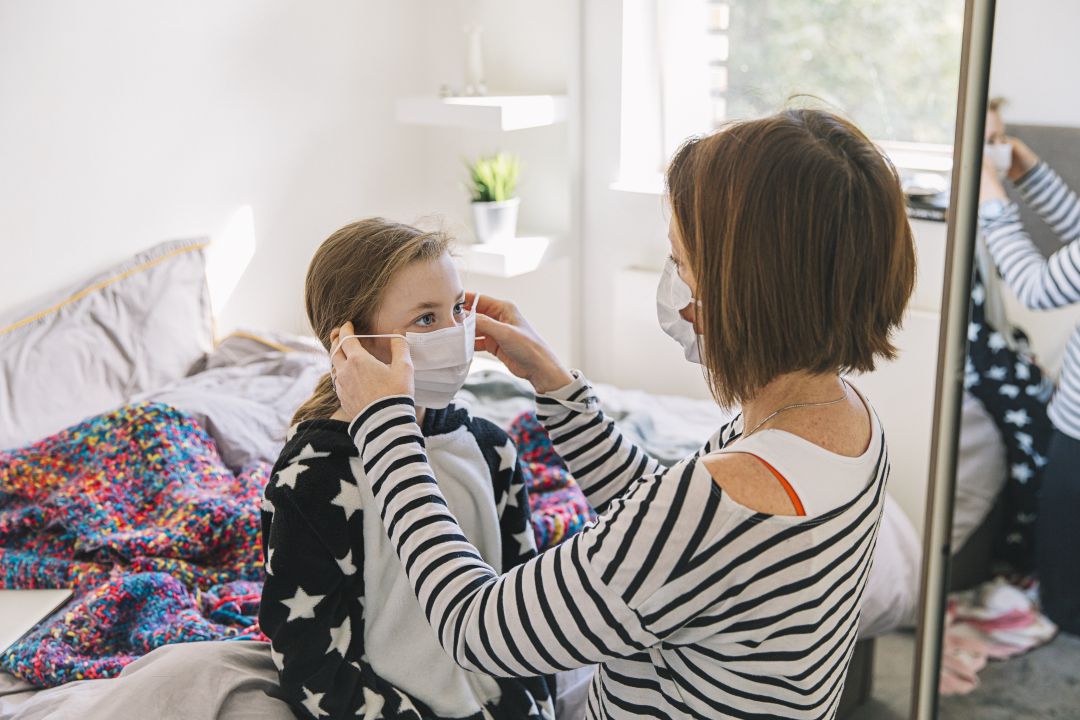 Una madre coloca una mascarilla a su hija en casa Una madre coloca una mascarilla a su hija en casa