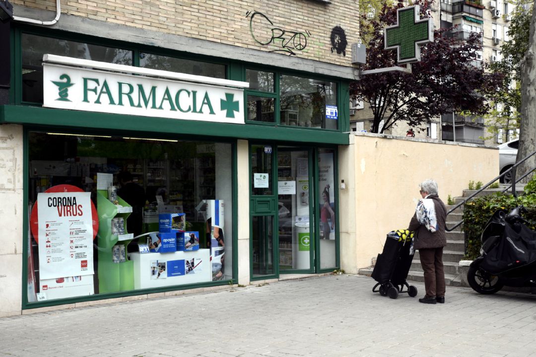Una mujer espera en la calle como medida de precaución a entrar en una farmacia Una mujer espera en la calle como medida de precaución a entrar en una farmacia