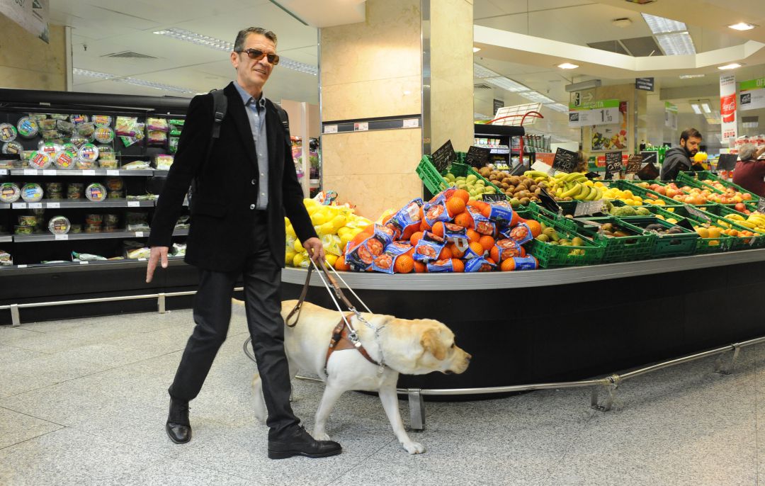 Un invidente camina con su perro guía por un supermercado. Un invidente camina con su perro guía por un supermercado.