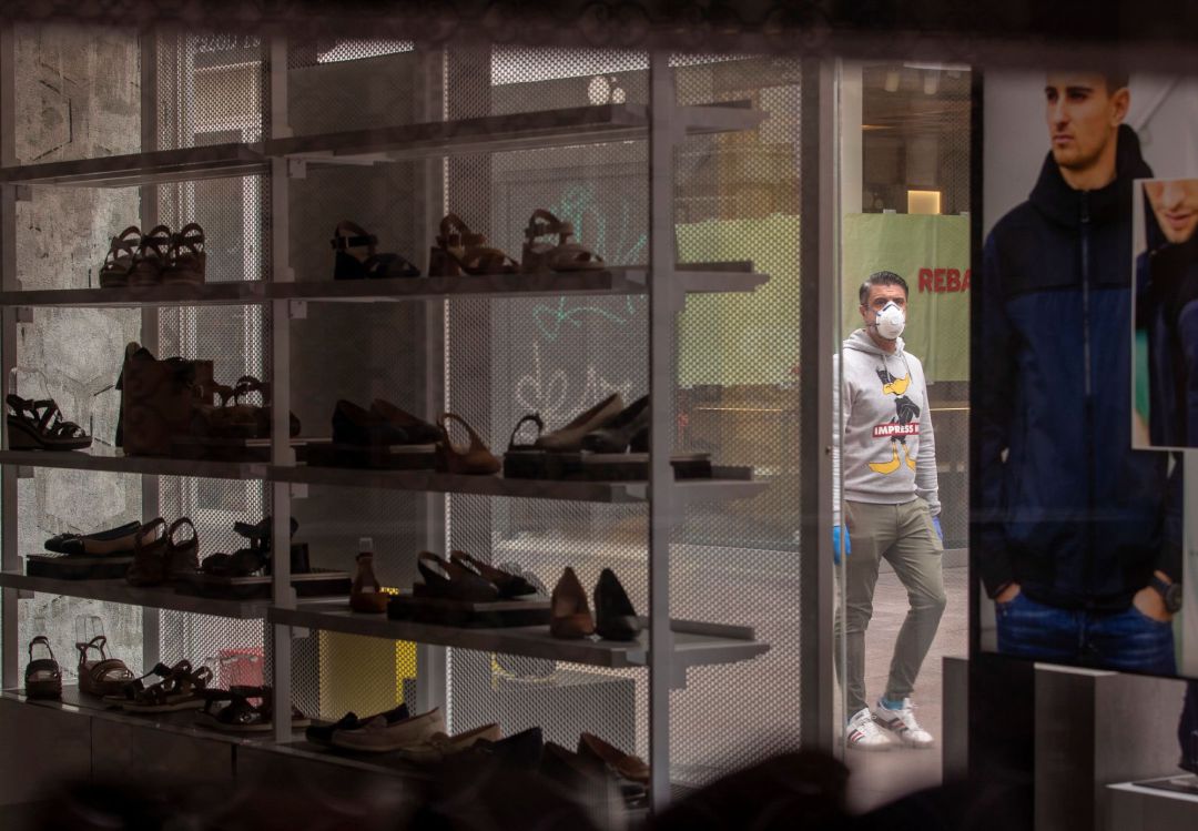 Un hombre protegido con mascarilla visto a través del escaparate de una tienda de zapatos cerrada. Un hombre protegido con mascarilla visto a través del escaparate de una tienda de zapatos cerrada.